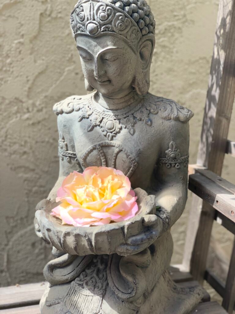 Stone Buddha statue holding a pale pink rose in cupped hands